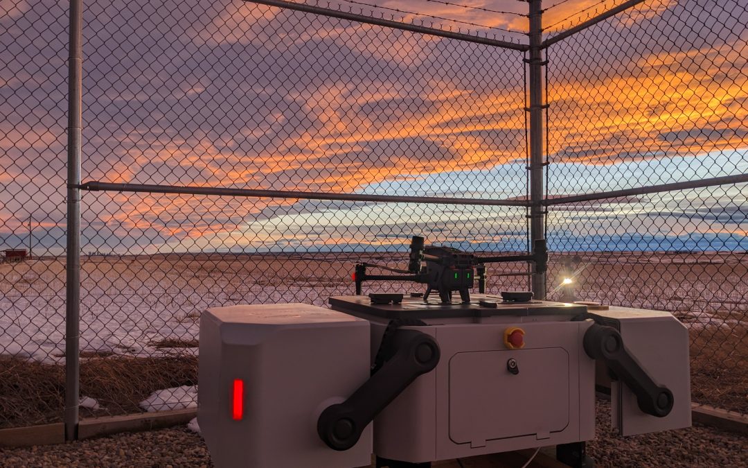 DJI drone docking station set behind fence. Background is facility site with a sunset
